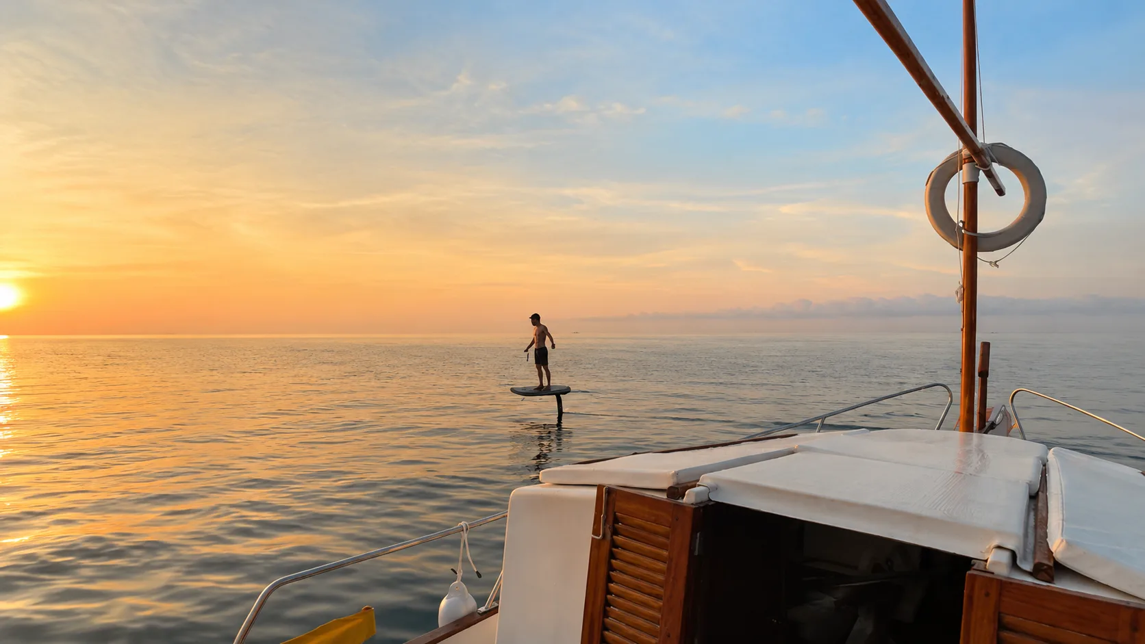 Guy foiling at sunrise with our traditional Menorcan llaüt boat.